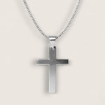 Silver cross pendant on a chain against a light gray background