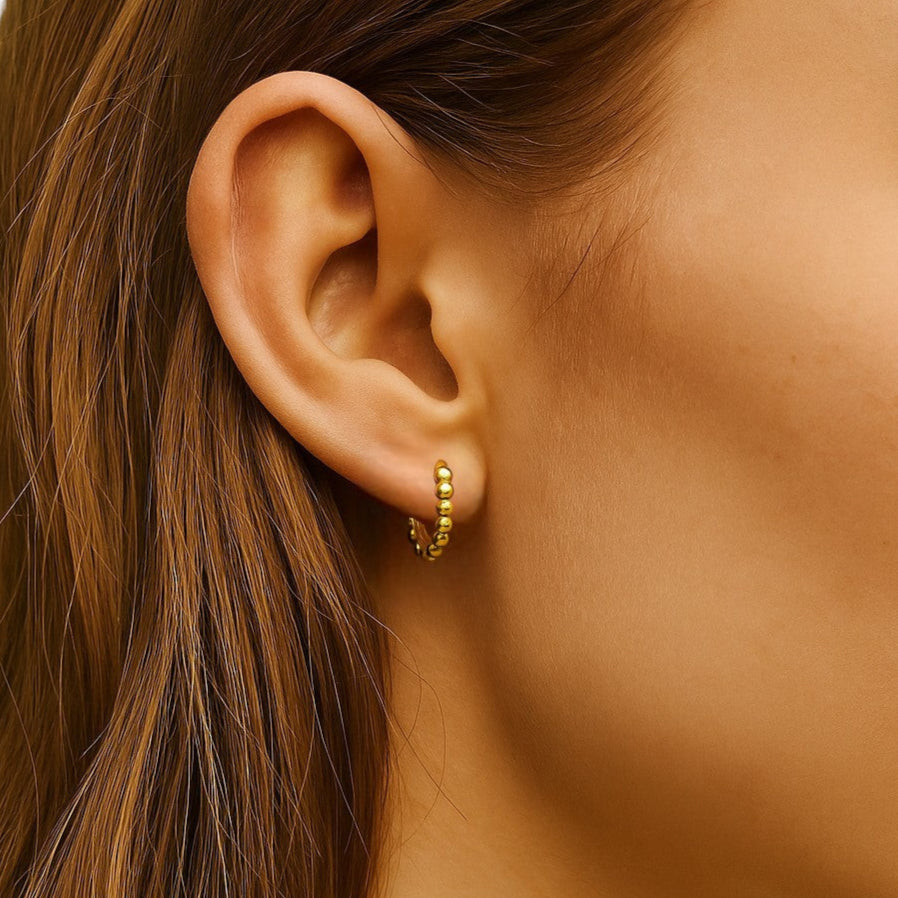 Close-up of an ear wearing a gold earring with hair partially obscuring the view.