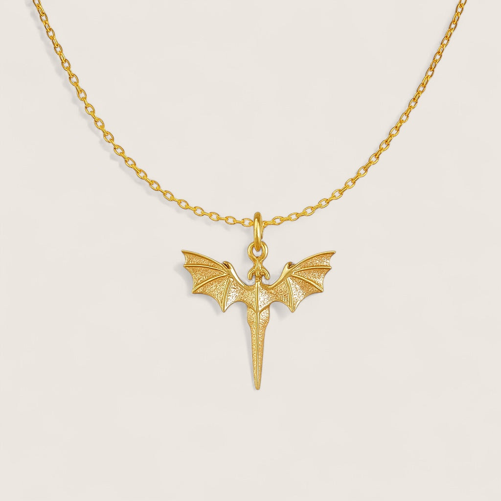 Gold necklace with a dragon-shaped pendant on a light beige background